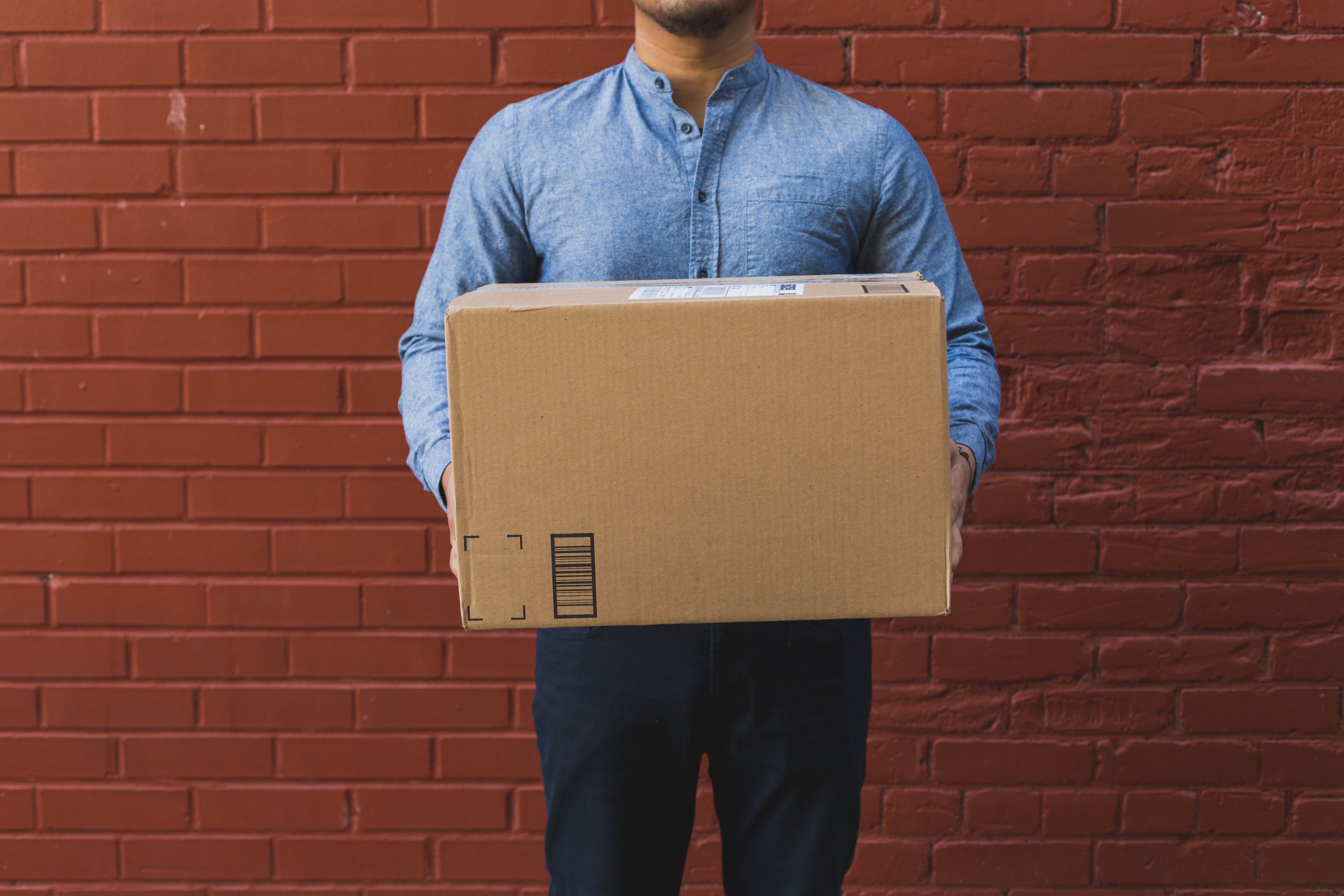 man-holding-shipping-box-on-red-brick